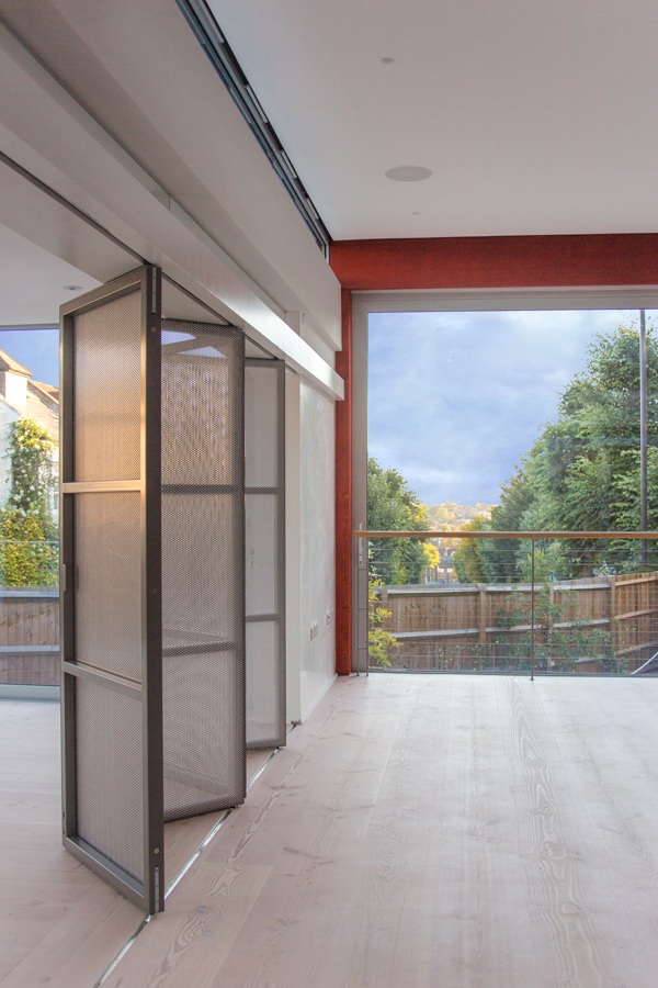 sliding folding screen of perforated metal panels separating living and drawing room