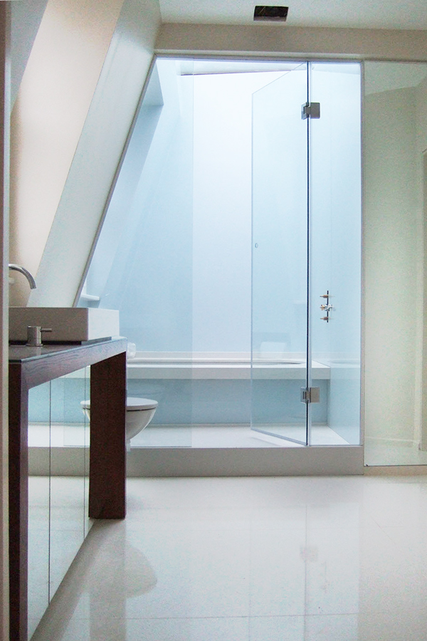 Wooden counter with a mirror on it and marble walls beside walk-in shower