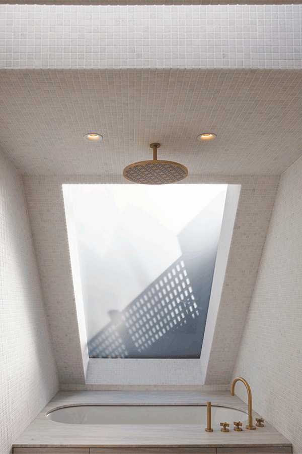 Undermounted bath beside skylight surrounded by stone mosaic