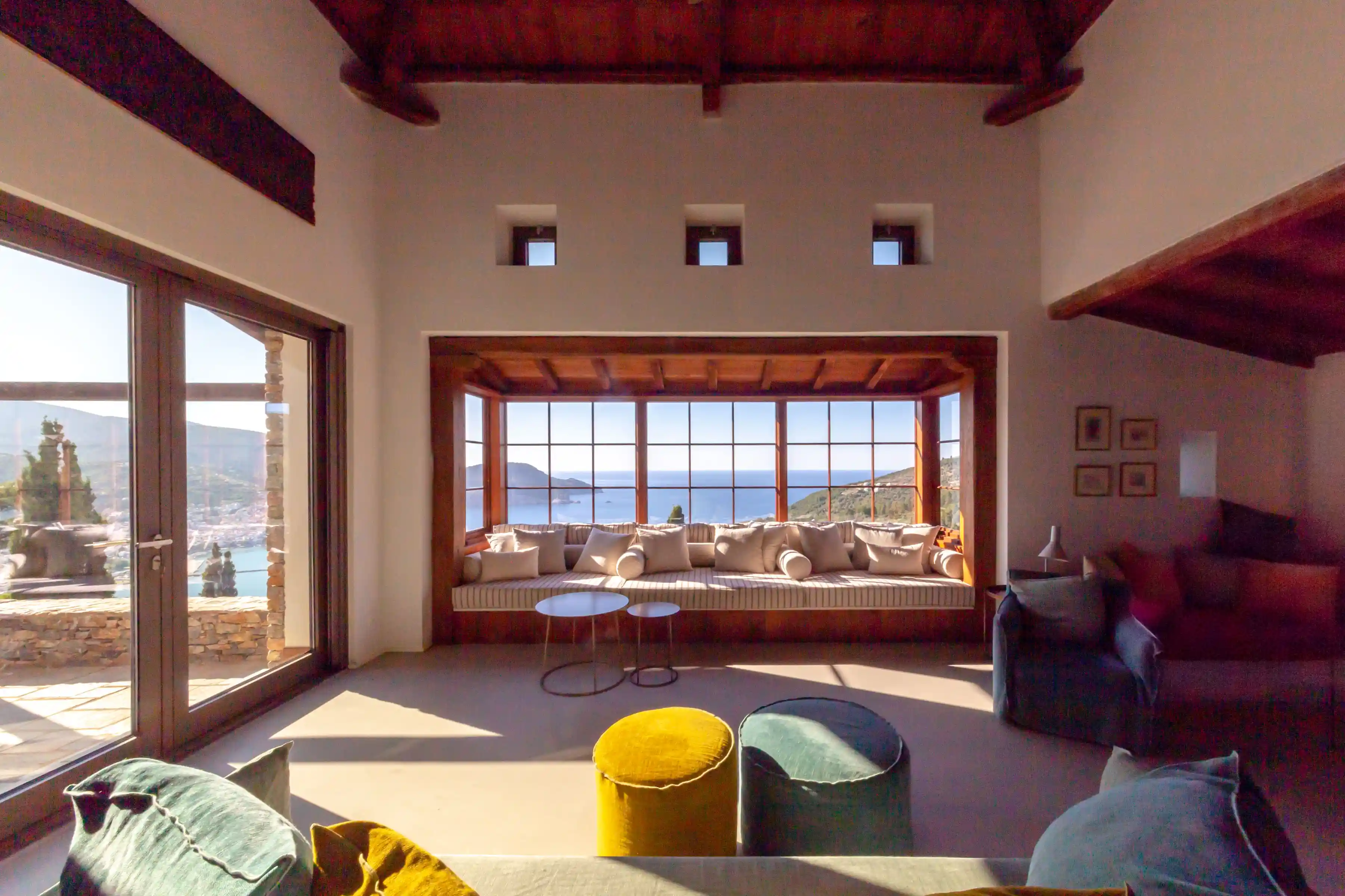 Three Stone Houses Skopelos - Living Room of the large house, looking towards the panoramic bay window seating, with winter fireplace nook to the right