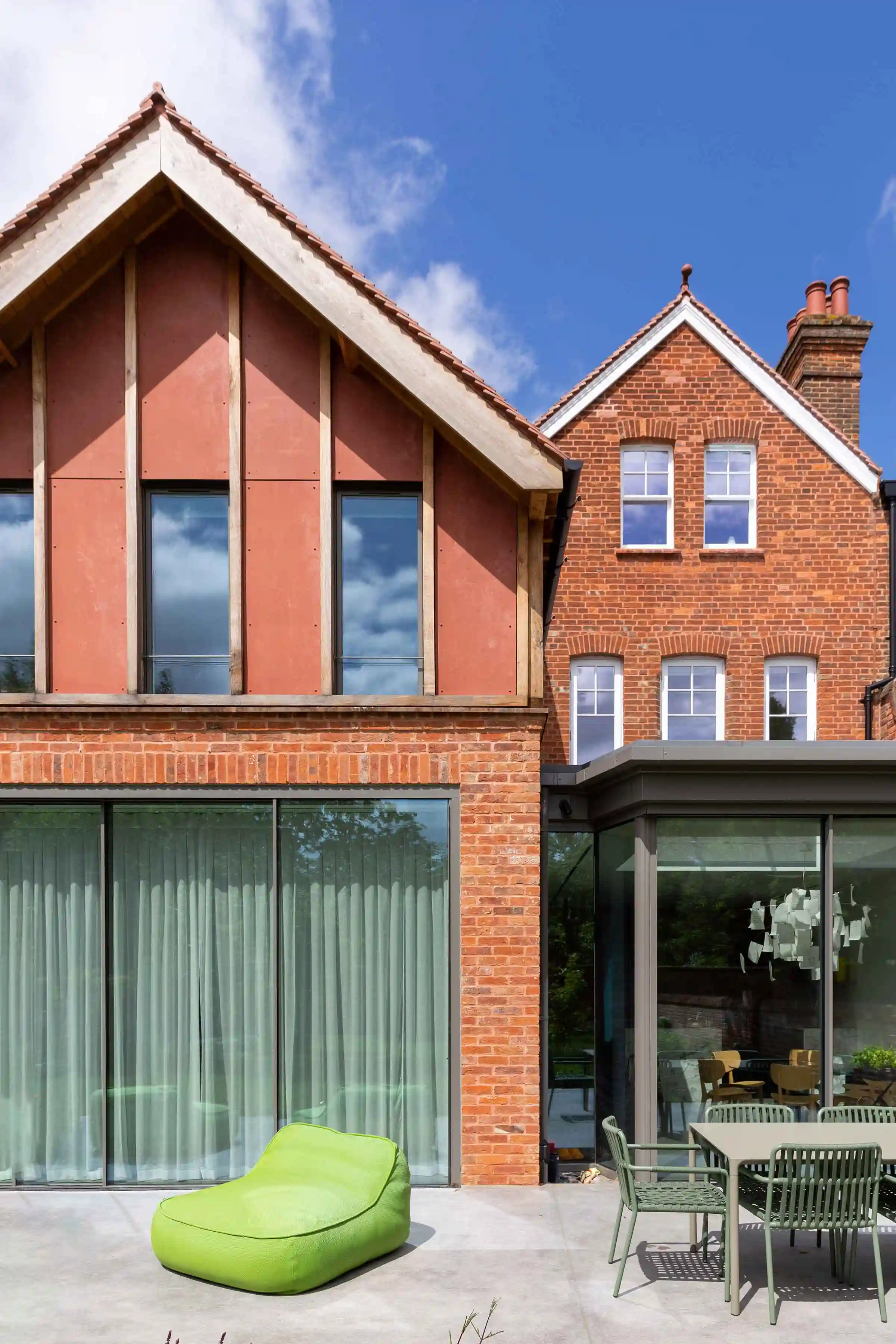Close-up of the new upper storey rear extension at Staverton Road Oxford — grid of red cement board panels framed by oak beams, large sliding glazed doors below