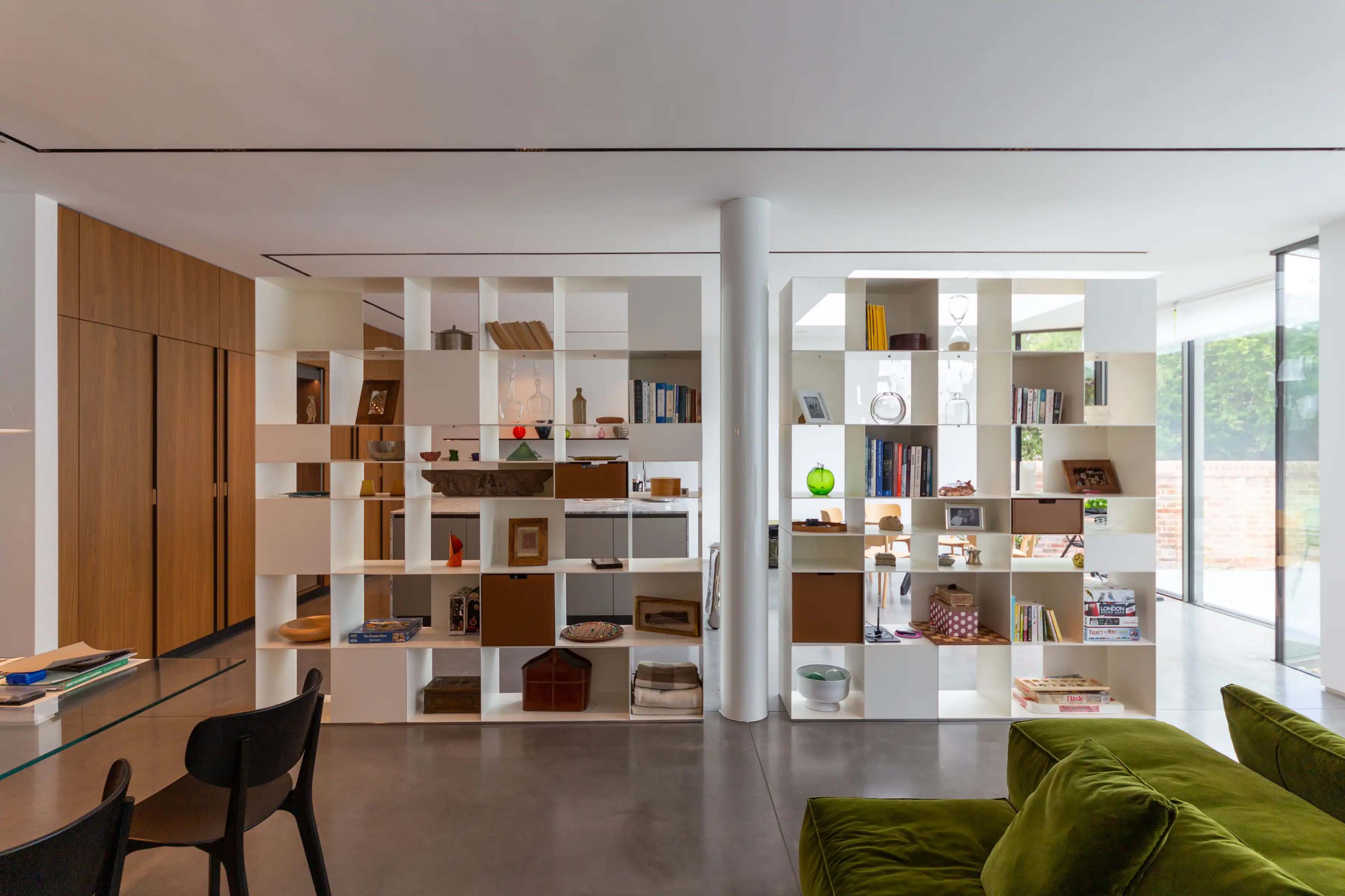 Open plan living space at Staverton Road Oxford — Antonio Citterio for Flexform shelving system dividing kitchen from lounge, green velvet sofa, garden views beyond glazed wall