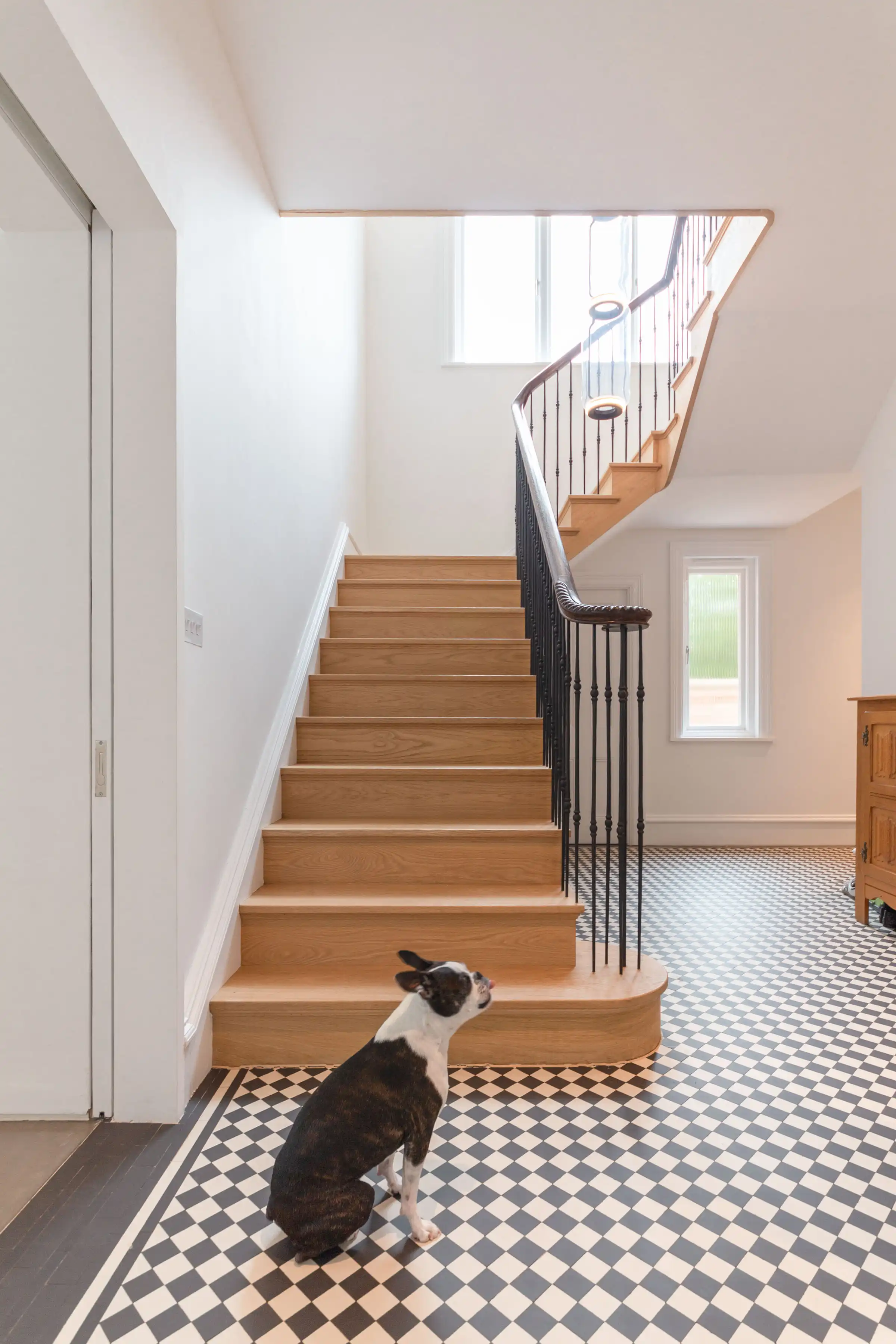 Entrance hall at Staverton Road Oxford — recreated oak staircase with black iron spindles and curved handrail, black and white encaustic Edwardian floor tiles, Flos Noctambule light column