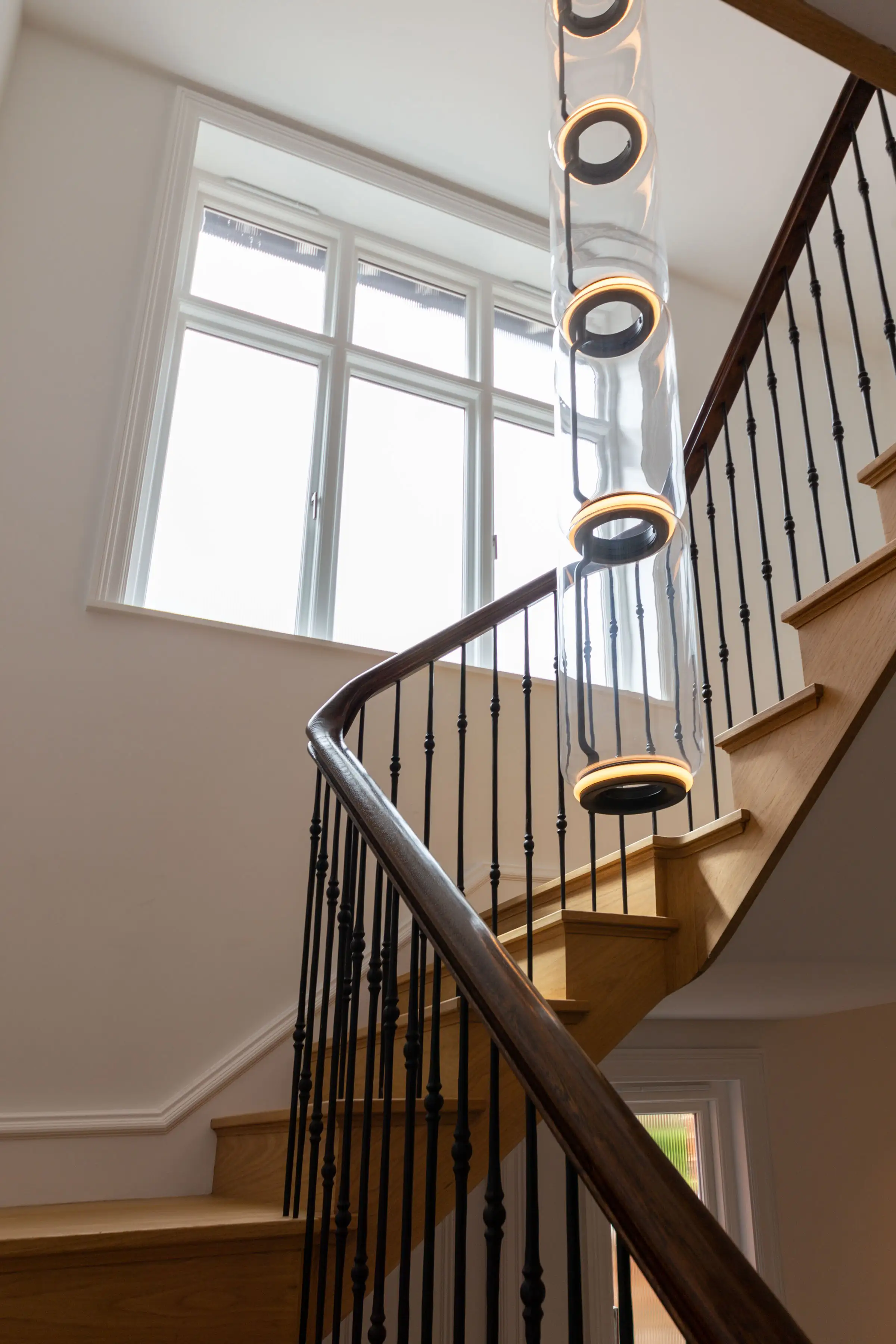 Staircase detail at Staverton Road Oxford — looking up the curved oak stair with black iron spindles and Flos Noctambule glass column pendant light
