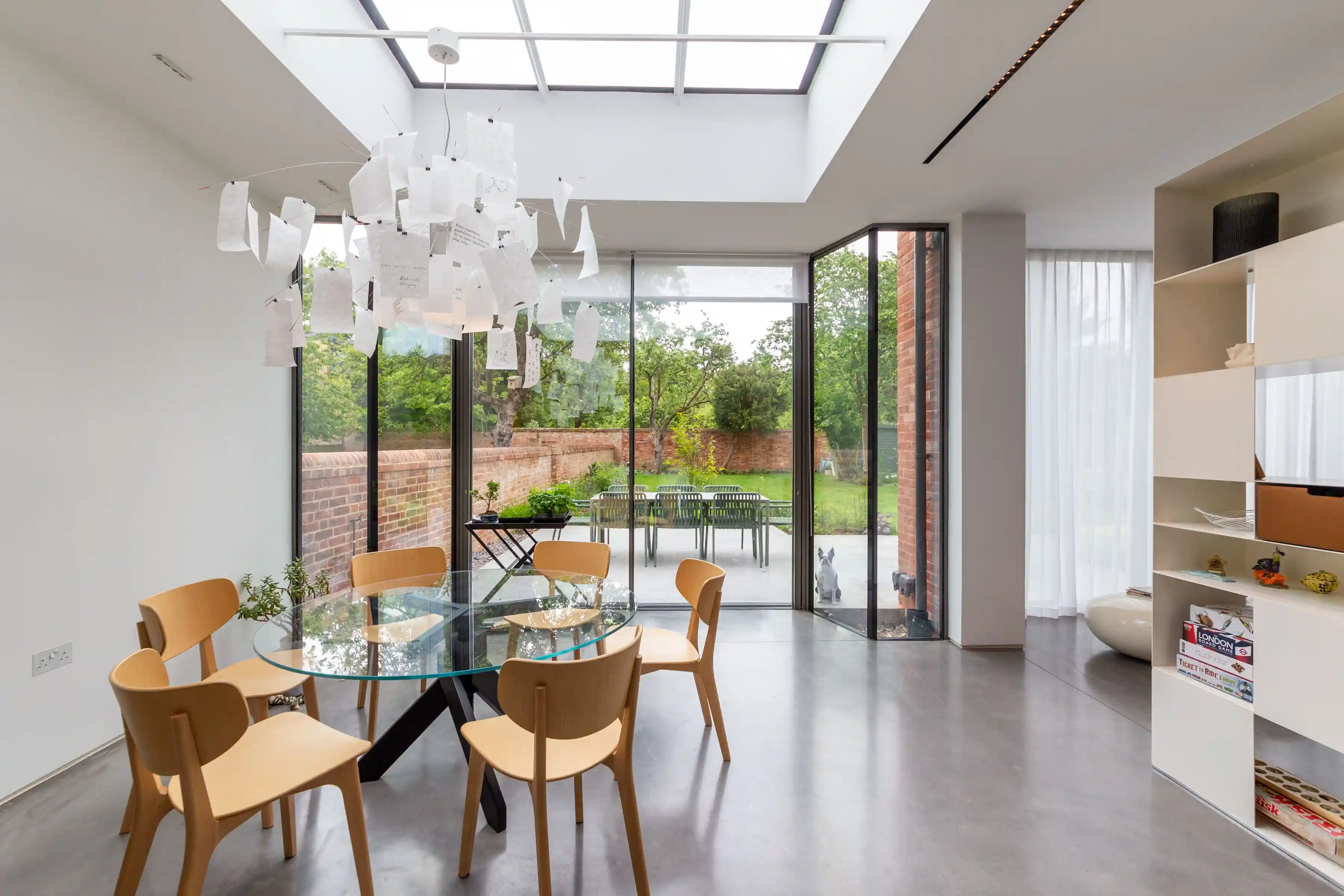New ground-floor extension at Staverton Road Oxford — dining area with round glass table, Flos pendant light, full-height glazed sliding doors opening to south-facing garden