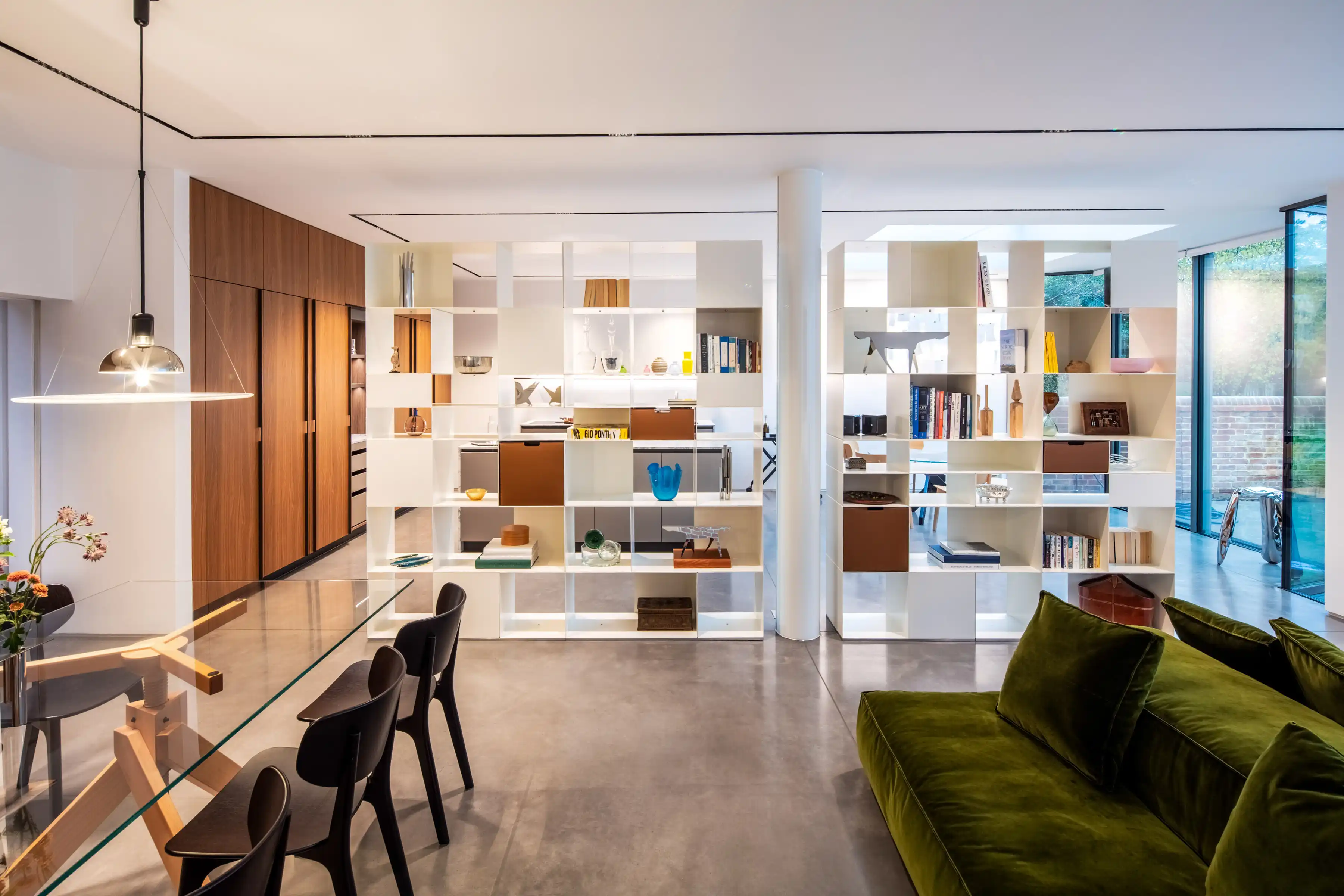 Open plan living space at Staverton Road Oxford — Antonio Citterio for Flexform shelving system dividing kitchen from lounge, green velvet sofa, garden views beyond glazed wall
