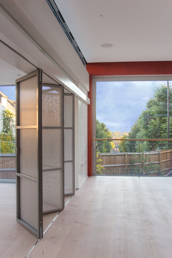 Sliding folding screen of perforated metal panels separating living and drawing room