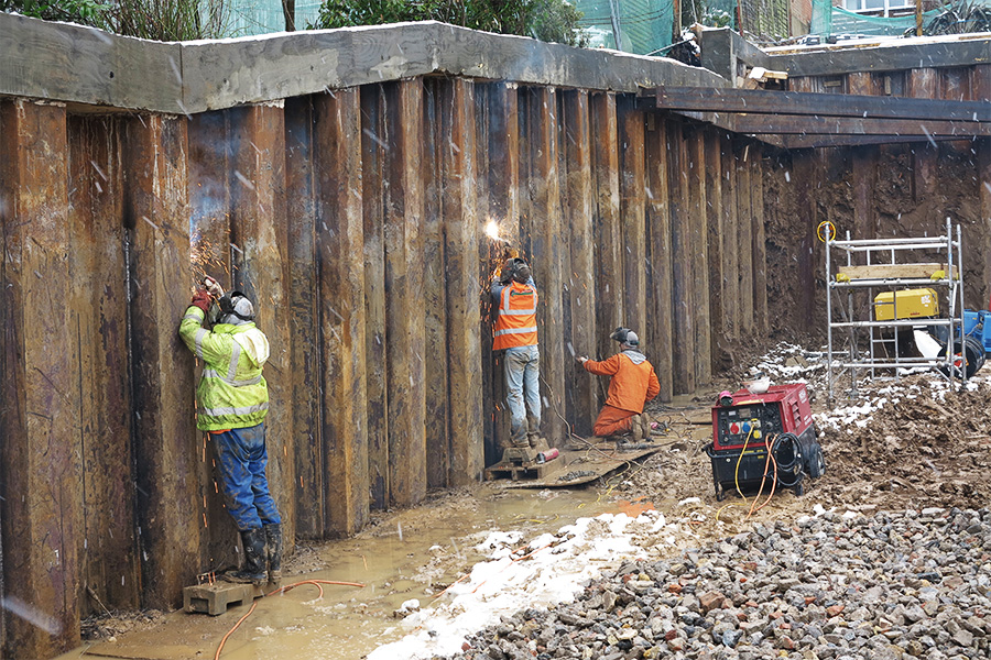 Below, the site has been excavated to reveal the piled retaining wall
